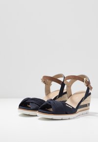 Námořnické látkové klínové sandály s uzlem vpředu, opasky na kotníku v barvě tan a bílými gumovými podešvemi; zahrnují také detail z tkané juty na podpatku.