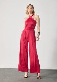 Rød halterneck jumpsuit med bred ben-design, med en indsyet talje og glat, letvægtsstof, suppleret af sorte strophæle.