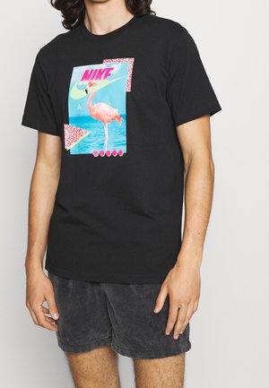 Schwarzes Baumwoll-T-Shirt mit einem bunten Flamingo-Motiv und dem Nike-Logo, akzentuiert durch lebendige geometrische Formen. Kurze Ärmel und lässiger Schnitt.