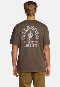 Rudas medvilninis marškinėliai su dideliu baltu gyvatės piešiniu ir užrašu "BILLABONG" bei "FEELING FREE SINCE 1973" nugaros pusėje. Trumpi rankoviai.