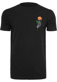 Camiseta de algodón negra con un gráfico de una mano esquelética sosteniendo una rosa rosa, con hojas verdes, en la parte izquierda del pecho.