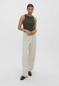 Débardeur côtelé vert olive associé à un pantalon large beige clair, avec des plis et des chaussures noires. Design simple et ajusté.