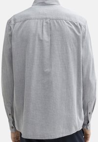 Chemise grise à manches longues avec une texture à motifs, dotée d'un col pointu et d'un ourlet droit. La vue arrière montre des plis pour un ajustement de la coupe.