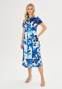 Blauwe jurk met bloemenprint, korte mouwen, geplooide rok en contrasterende top. De stof lijkt lichtgewicht met een gladde textuur.