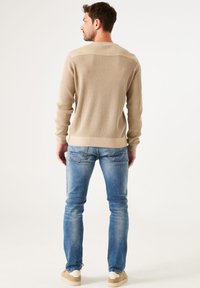 Pull beige à côtes avec des manches longues et un col rond. Assorti à un jean skinny bleu délavé et des baskets beiges.