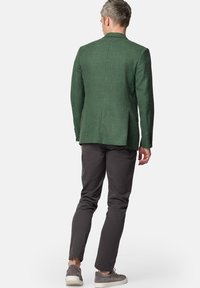 Zielony żakiet o fakturze i dopasowanym kroju, zestawiony z ciemnoszarymi spodniami i jasnoszarymi butami sportowymi. Wyraziste szwy na ramionach i rozcięcie z tyłu.