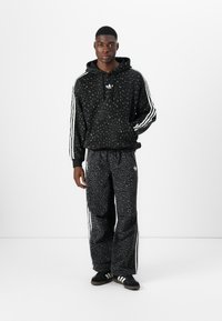 Svart hoodie med leopardmönster, vita ränder på ärmarna; matchande svarta sweatpants med leopardmönster; båda i mjukt material; avslappnad passform.