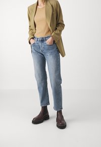 Jasnoniebieskie dżinsy straight-leg zestawione z beżowym prążkowanym topem i oliwkowym żakietem. Brązowe botki za kostkę z grubą podeszwą.