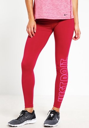Leggings rouges avec une texture lisse et une coupe ajustée, arborant l'inscription "JUST DO IT" en rose clair sur la jambe gauche.