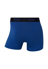Blå bomuldsboxershorts med sort elastisk linning med teksten "CRISTIANO" i lilla. Glat tekstur, tætsiddende design.
