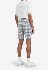 Men's plaid shorts in light blue, tan, and white. Features a back pocket with button closure and a label, made from lightweight fabric.