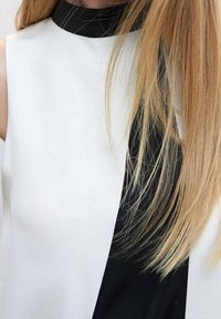 Débardeur sans manches avec un col haut, design structuré en tissu noir et blanc. Texture lisse avec un contraste de couleurs audacieux.