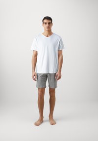 T-shirt bianco in cotone con maniche corte e scollatura a V abbinato a pantaloni corti grigi in cotone. La vestibilità è rilassata e il tessuto sembra morbido. Nessun motivo visibile.