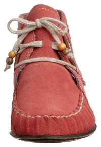 Červený mokasín z broušené kůže s prošitými detaily, zaoblenou špičkou a béžovou šňůrkou s dřevěnými korálky. Texturovaná podrážka.