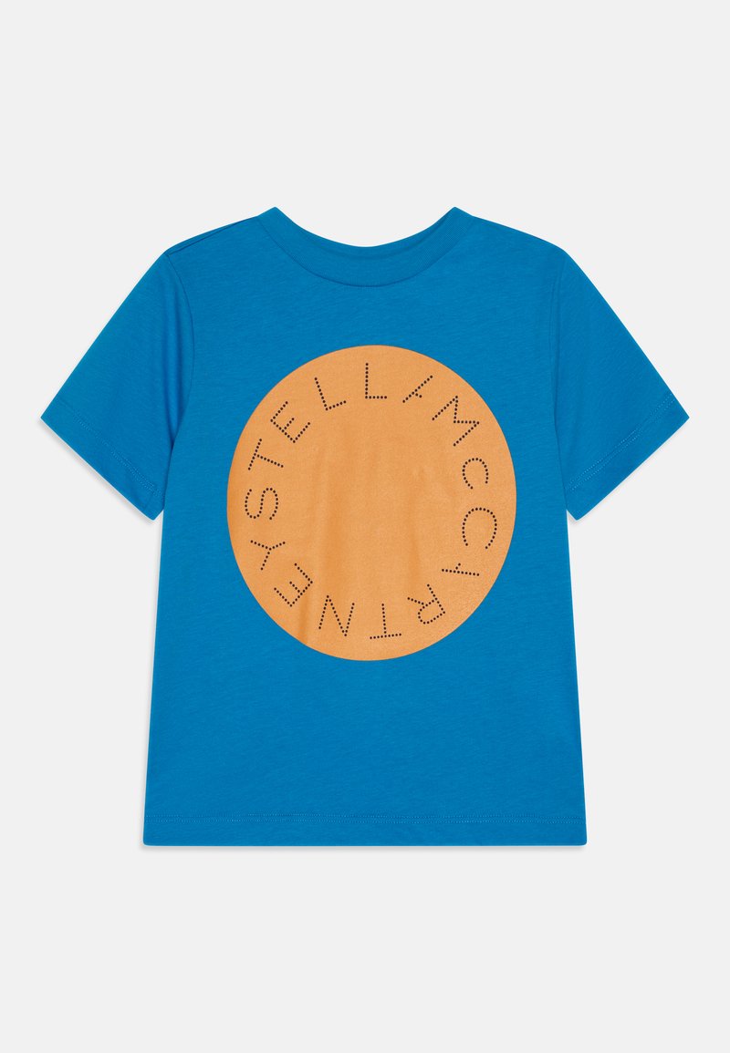 Blå bomullströja med en stor orange cirkulär grafik med texten "STELL/MCCARTNEY" i prickmönster. Korta ärmar, rundad hals.