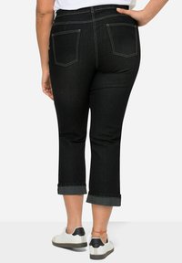 Mustat denimiin perustuvat lyhyet housut, joissa on käänteet, kaksi takataskua ja kontrastia ompelu, yhdistetty valkoisiin ja mustiin lenkkareihin.