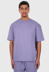 Lys lilla oversized T-skjorte laget av mykt stoff med rund hals og korte ermer. Har et lite merke på kanten.