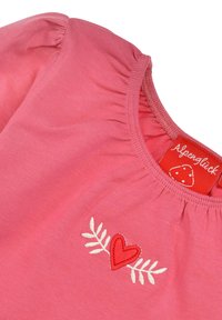 Rosa Baumwoll-Bluse mit gerafftem Halsausschnitt, gesticktem roten Herz und Blättern. Etikett im Kragenbereich sichtbar.