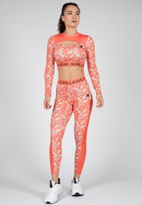 Koraal atletische set met een lang mouw crop top met uitsparing en bijpassende leggings. Beide hebben een camouflagedessin en zwarte merkaccenten.