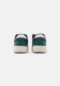 Sneakers verdi e neri con tomaia in pelle texturizzata, accenti bianchi a contrasto e suola in gomma beige, visti da dietro.