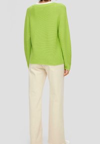 Leuchtend grüner, gerippter Strickpullover mit einem weißen Kragen, kombiniert mit cremefarbigen, geraden Hosen. Verfügt über eine lockere Passform und ein strukturiertes Material.