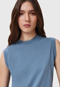 Top senza maniche di colore azzurro chiaro realizzato in tessuto morbido; presenta un collo alto e un design minimalista privo di motivi o decorazioni.