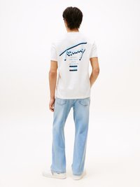 Vit t-shirt med kort ärm och blå grafisk text på baksidan, kombinerad med ljusblå vida jeans och vita sneakers.