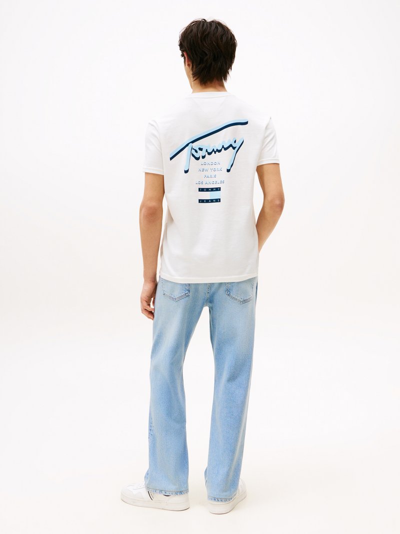 Vit t-shirt med kort ärm och blå grafisk text på baksidan, kombinerad med ljusblå vida jeans och vita sneakers.