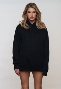 Black oversized hoodie made of soft fabric, featuring a front pocket, drawstring hood, and ribbed cuffs. Simple, monochromatic design.