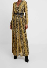 Robe longue plissée jaune et noire avec un motif serpent, dotée d'un décolleté en V profond et de manches longues, cintrée à la taille par une ceinture noire.