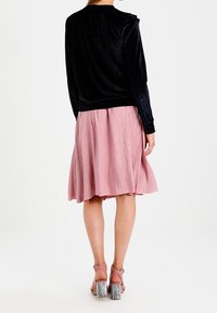 En svart sammets långärmad topp i kombination med en rosa knälång kjol. Kjolen har en veckad design och en flödande silhuett. Bärs med rosa klacksandaler.