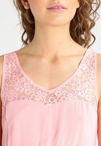 Rosa ärmlös topp med spetsinsats vid halsringningen som har blommönster, mjuk textur och avslappnad passform.