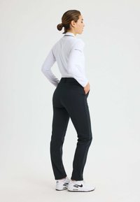 Witte lange mouwen shirt met zwart kraagdetail, gecombineerd met aansluitende zwarte broek. Model draagt witte sneakers met zwarte accenten.