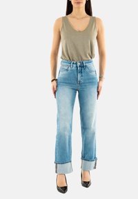 Top sin mangas gris claro con escote en V, combinado con jeans de tiro alto azul claro, con puños doblados y zapatos de tacón negro.