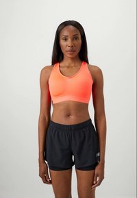 Sutiã desportivo laranja-neon com uma textura suave e alças largas, combinado com calções de desporto pretos com um cós elástico e um pequeno logótipo.