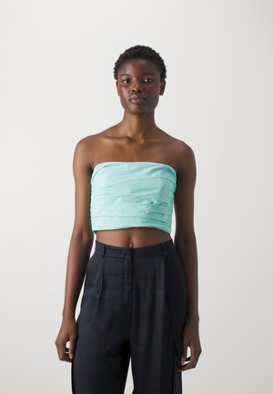 Light turquoise strapless top with gathered texture, worn with high-waisted navy trousers featuring side pockets and a smooth finish.