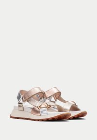Metalliset sandaalit, joissa on rose gold, hopea ja valkoiset hihnat. Varustettu tekstuuripinnalla, säädettävillä hihnoilla ja ruskealla kumipohjalla.
