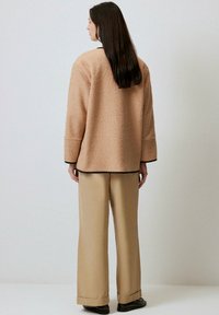 Giacca beige con texture, dal taglio morbido e maniche ampie, abbinata a pantaloni beige a gamba larga e calzature nere. Design semplice con finiture a contrasto.