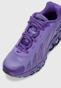 Ljubičaste trkačke cipele s teksturiranim, reflektirajućim gornjim dijelom, istaknutim Nike logom i prepoznatljivim valovitim uzorkom. Imaju vezice i podstavljeni potplat.
