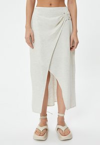 Lichtbeige wikkelrok in een zachte, textuurstof met een zijdelingse ruchingdetail en een hoge split tot boven de dij. Gekocht met beige sandalen.