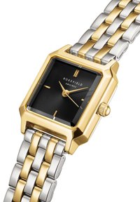 Orologio in metallo dorato e argentato con quadrante quadrato nero, caratterizzato da motivi testurizzati, indici delle ore dorati e una corona di lato.