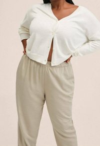 Lichtbeige cardigan met een diepe V-hals, knopen aan de voorkant en geribde manchetten, gecombineerd met losse lichtgrijze broek met een elastische tailleband.