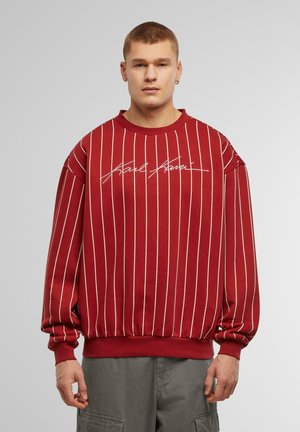 Sweatshirt rouge avec des rayures verticales blanches, col rond et manches à poignet ; affiche un logo en écriture sur la poitrine ; fabriqué en tissu doux.