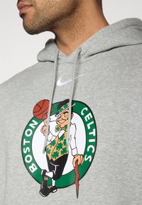 Γκρι φούτερ με κουκούλα που φέρει το λογότυπο των Boston Celtics, με μια φιγούρα λεπρετσίνου που κρατάει μι α μπάλα του μπάσκετ, διακοσμημένο με πράσινες και λευκές λεπτομέρειες.