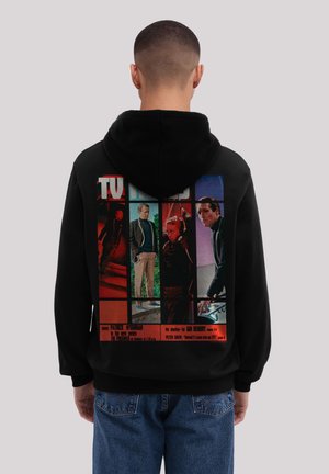 Back view of a person wearing a black hoodie featuring a multicolor vintage TV Times magazine cover with four male actors printed on the back.