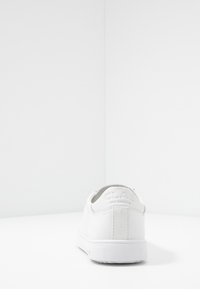 White leather sneaker with a low profile, rear pull tab, and embossed brand logo. Smooth texture and rubber sole with a textured tread pattern.