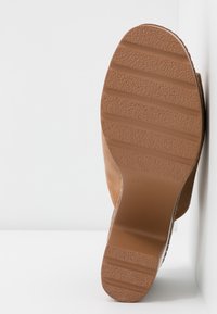 Semelle en daim marron avec une semelle extérieure en caoutchouc texturé, présentant des rainures horizontales pour une meilleure adhérence. Le talon est légèrement surélevé et arrondi.