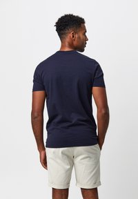 Dunkelblauses Baumwoll-T-Shirt mit kurzen Ärmeln, Rundhalsausschnitt und glatter Textur, kombiniert mit hellbeigen hochgerollten Shorts.