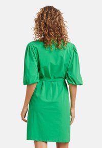 Groene jurk met pofmouwen, een gecincht middel en een lengte tot de knie. Soepele stof met een effen kleur en minimale details.