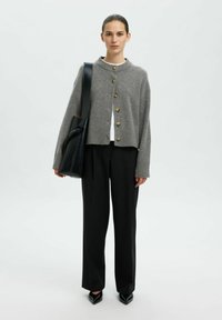 Grauer Wollcardigan mit Rundhalsausschnitt und Knopfverschluss, kombiniert mit schwarzen maßgeschneiderten Hosen und schwarzen spitzen Pumps.